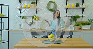 Young attractive woman in positive mood is dancing in kitchen, wearing wireless headset, listening music, having fun at