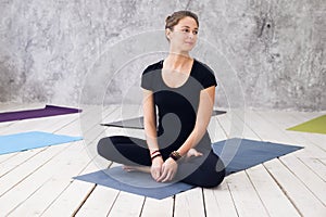 Young attractive woman practicing yoga, sitting in Ardha Padmasana exercise, Half Lotus pose, working out, wearing black