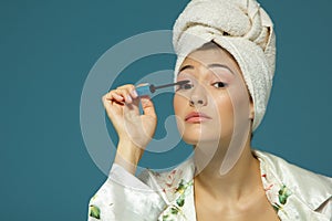 Young attractive woman putting eye mascara over blue background