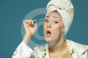 Young attractive woman putting eye mascara over blue background