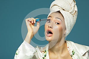 Young attractive woman putting eye mascara over blue background