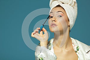 Young attractive woman putting eye mascara over blue background