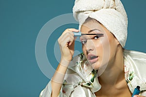 Young attractive woman putting eye mascara over blue background