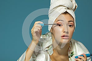 Young attractive woman putting eye mascara over blue background