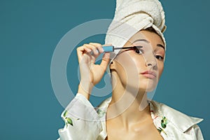 Young attractive woman putting eye mascara over blue background