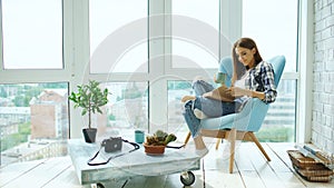 Young attractive woman read book and drink coffee sitting on balcony in modern loft apartment