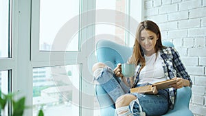 Young attractive woman read book and drink coffee sitting on balcony in modern loft apartment