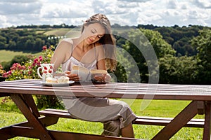 Young attractive woman, reading a book outdoor, enjoying coffee