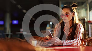 Young attractive woman in red sunglasses with tablet computer sitting in cafe. Beautiful girl in airport or shoppping