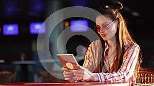 Young attractive woman in red sunglasses with tablet computer sitting in cafe. Beautiful girl in airport or shoppping