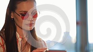 Young attractive woman in red sunglasses using tablet computer with touchscreen in a cafe. Beautiful girl in airport or