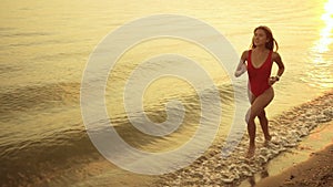 Young attractive woman in red swimsuit is running on sandy sea beach at sunset.