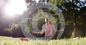 The young attractive woman is resting in the park. The woman is meditating in the lotus pose