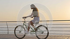 Young attractive woman riding vintage bike near the sea during sunrise or sunset