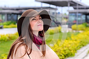 Young attractive woman in sandy coat and brown hat on, a breath of fresh air in a city Park on the waterfront