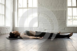 Young attractive woman in Savasana pose, white loft studio backg