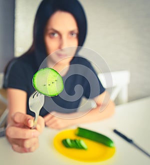 Young attractive woman show cucumber on fork