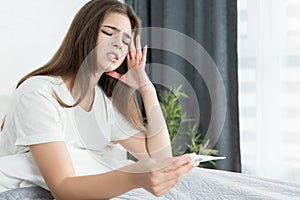 Young attractive woman sitting in bed with termometer in her hands feeling sick early in the morning photo