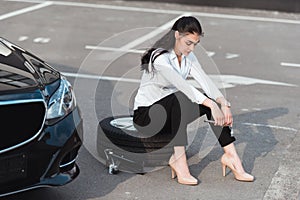 Young attractive woman sitting on car tire with lug wrench in her hand