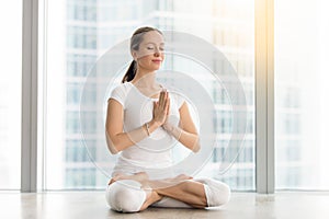 Young attractive woman sitting in Padmasana pose against floor w