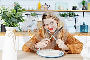 Young attractive woman sitting at table in kitchen with empty plate