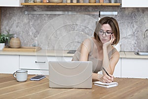 Young attractive woman sitting at the table and working on laptop in the kitchen at home