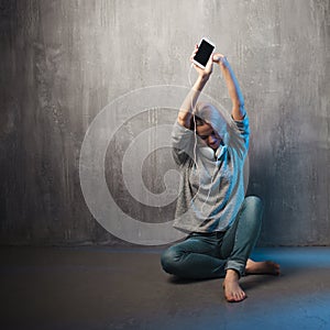 Young and attractive woman with smartphone and large headphones, sitting on the floor. Music in the mobile app.