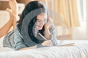 Young attractive woman smiling and drawing with pencil in notebook while lying on sofa