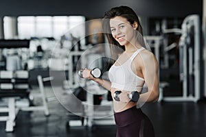 Young attractive woman in sport clothes holding weight dumbbell doing fitness workout in the gym