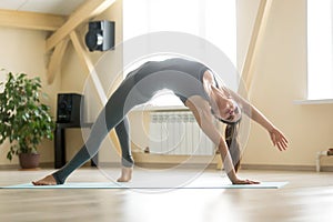 Young attractive woman standing in Camatkarasana pose, home inte