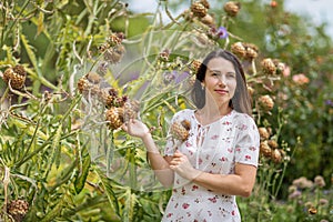 Young attractive woman standing near huge burdock plant in old overgrown park