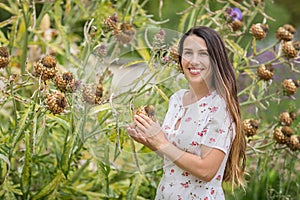 Young attractive woman standing near huge burdock plant in old overgrown park