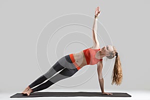 Young attractive woman standing in Side Plank pose, grey studio