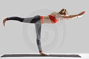 Young attractive woman standing in Warrior Three pose, grey stud