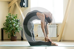 Young attractive woman stretching in Ustrasana pose, home interi