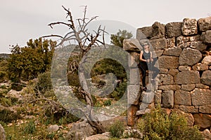 young attractive woman in sunglasses and with trekking poles against stone wall