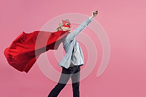 Young attractive woman superhero. Girl in a business suit and a mask with red cloak of hero.