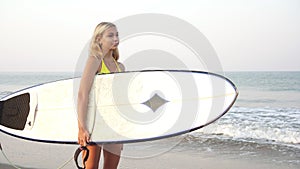 Young attractive woman surfer stands with a surfboard on the background of the sea