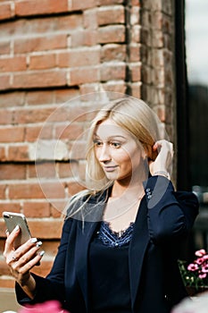 A young attractive woman takes a picture of herself on her smartphone, sitting on a street bench during the lunch break