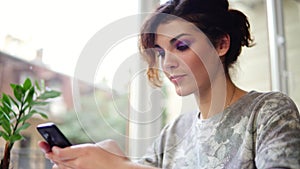 Young attractive woman texting on her mobile phone in cafe and smiling. Woman using app on smartphone in cafe drinking