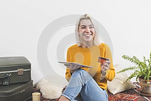 Young attractive woman using her credit card to make an online purchase with a digital touchscreen tablet at home