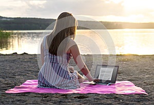 Young attractive woman using laptop on beach at sunset.