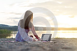 Young attractive woman using laptop on beach at sunset.