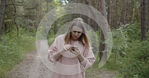 Young attractive woman using smartphone to navigate in a summer forest