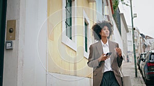 Woman using smartphone walking city street. African american girl looking phone.