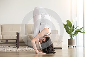 Young attractive woman in uttanasana pose, at hotel living room photo