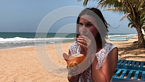 Young attractive woman on vacation sitting by sea, tropical beach, drinking cocktail in coconut, traveling in