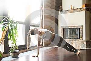 Young attractive woman in Vasisthasana pose, home interior backg