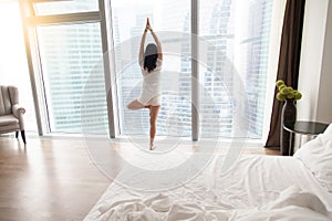 Young attractive woman in Vrksasana pose near the unmade bed