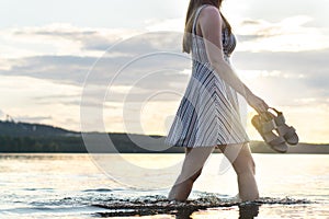 Young attractive woman walking in lake water at sunset.